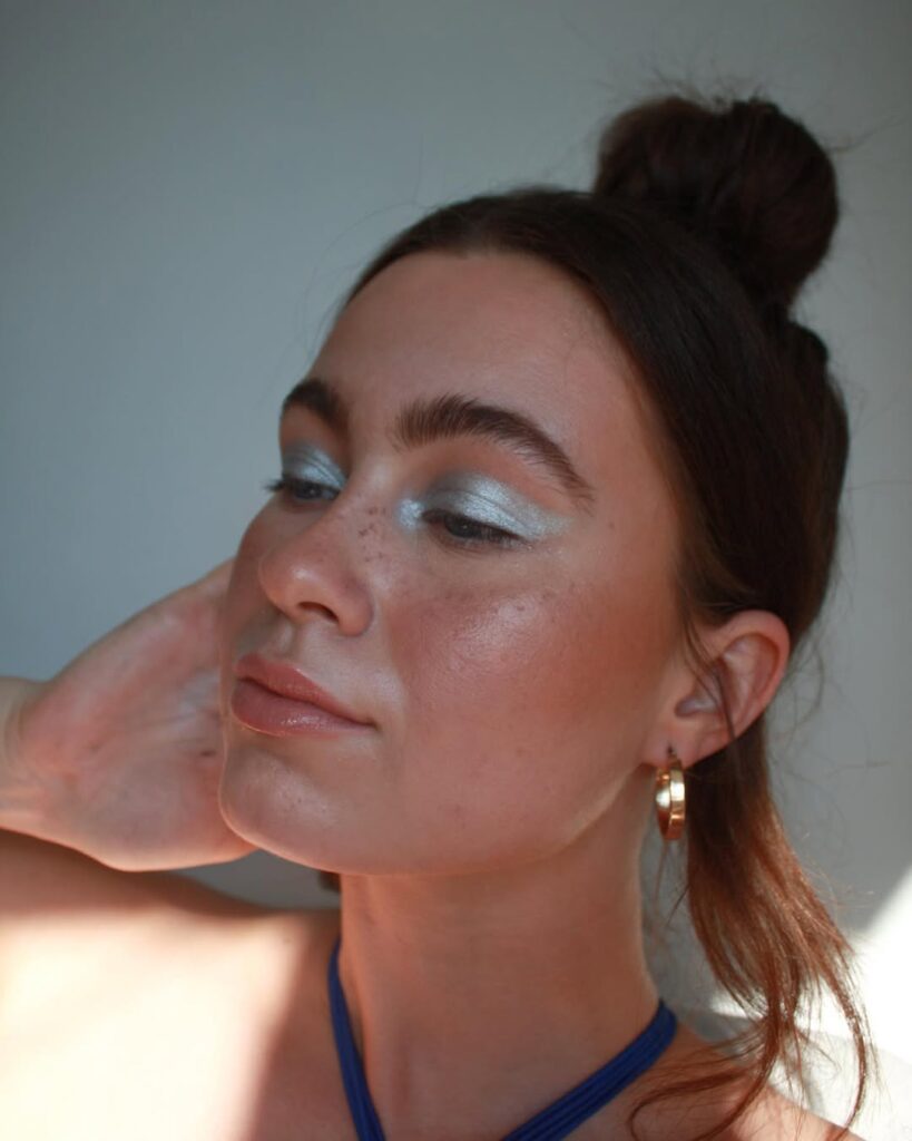 Mulher de pele clara, com cabelo meio preso e maquiagem com sombra azul metálica 