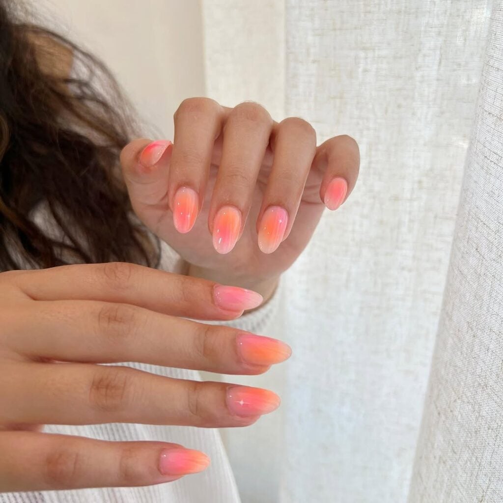 Mãos de pele clara, com unha aura laranja e rosa