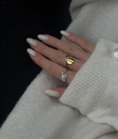Mão de pele clara, com anéis em dourado e unha amendoada perolada com strass