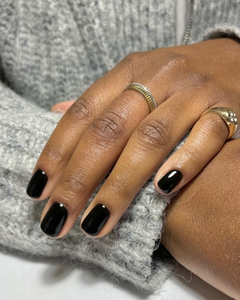Mão de pele preta, com anéis em dourado e unha curta com esmalte preto