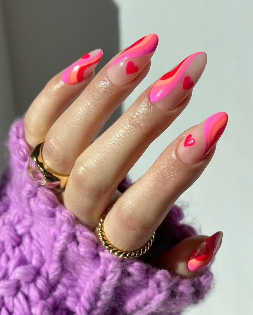 Mão de pele clara, com anéis em dourado e unha amendoada vermelho e rosa