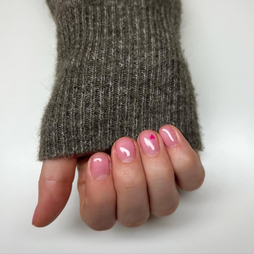 Mão de pele clara, com unha curtinha rosa-claro com coração 
