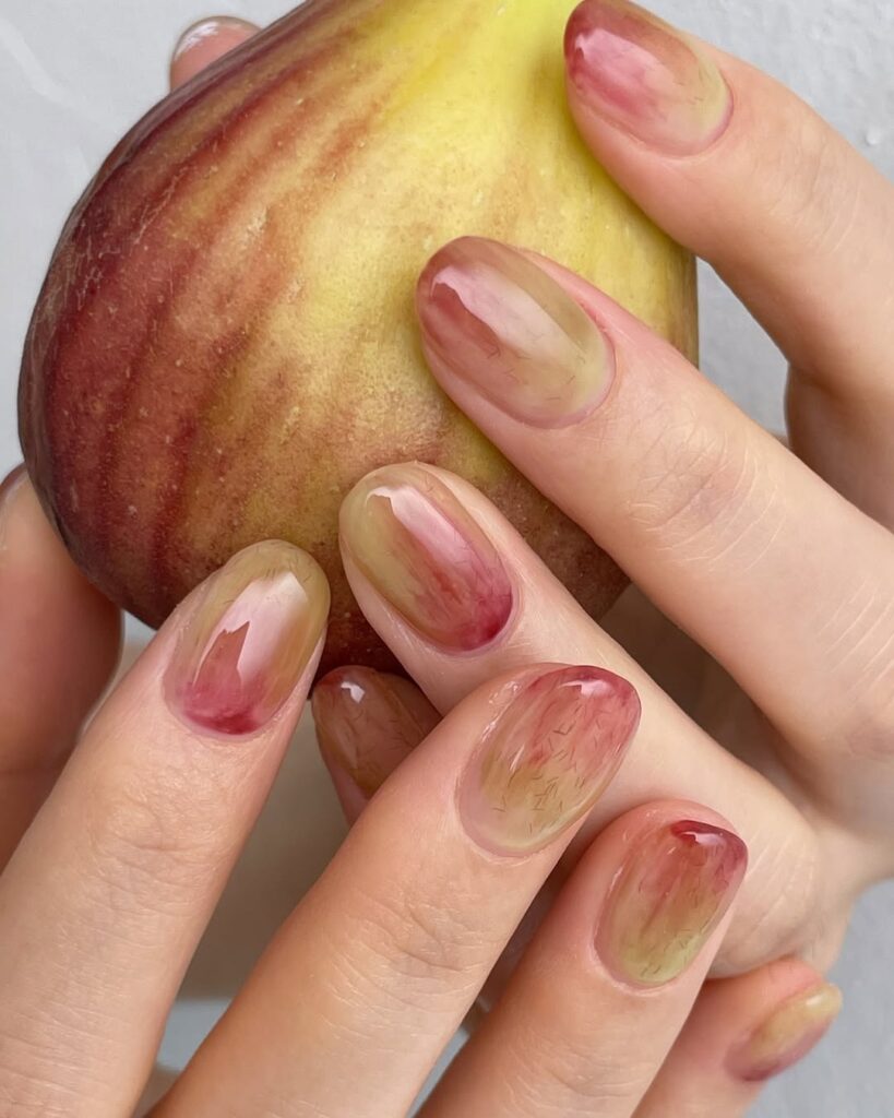 Mãos de pele clara, com unha redonda decorada com fruta