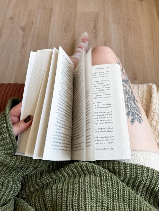 Mulher de pele clara, com tricot verde, sentada folheando um livro