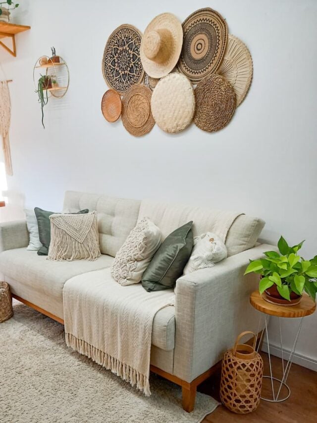 Sala com sofá cinza, manta e almofadas, e painel com itens de palha na parede