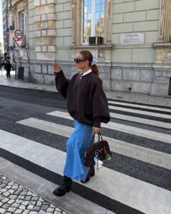 mulher jovem com suéter marrom, saia azul e bota marrom