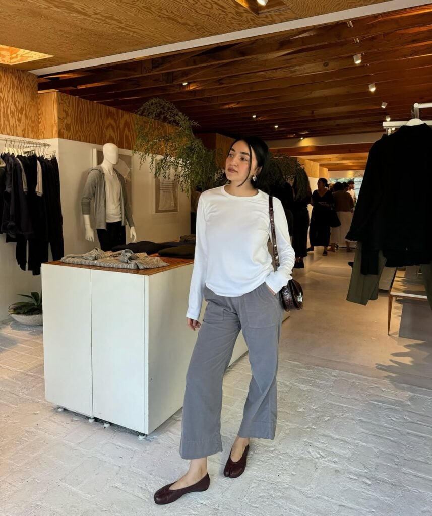 mulher jovem com blusa branca, calça cinza e sapato tabi marrom