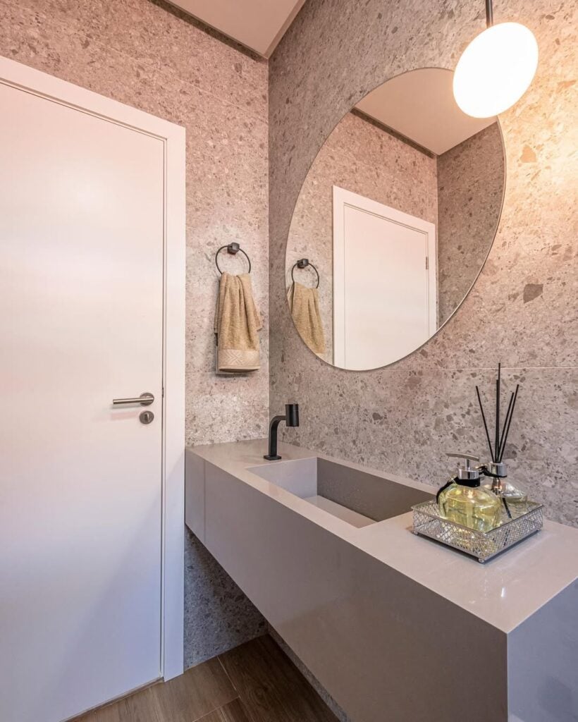 Banheiro com papel de parede, espelho redondo e bancada cinza com bandeja decorativa