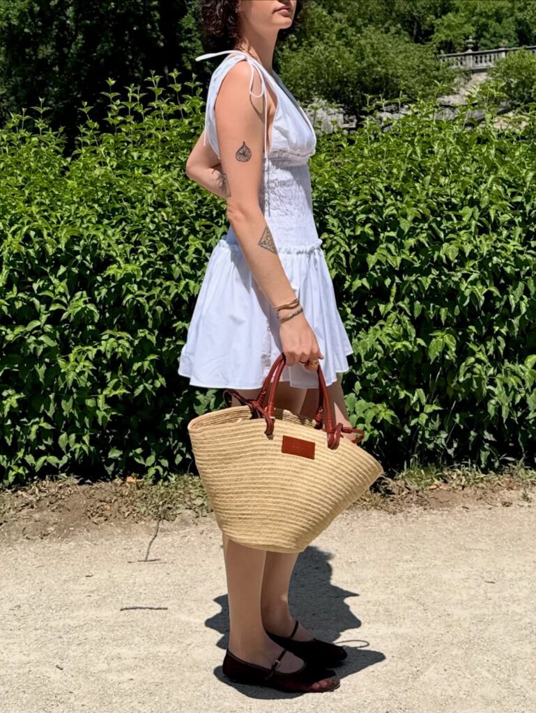 mulher com vestido branco curto, sapatilha e bolsa de palha