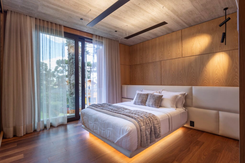 Quarto com parede e piso amadeirado com cama branca e cabeceira estofada