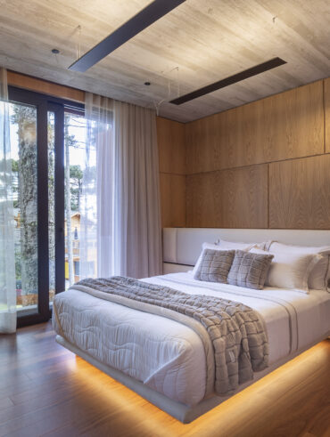 Quarto com parede e piso amadeirado com cama branca e cabeceira estofada