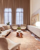 Sala de estar com sofá e poltronas em tons neutros, tapete de fibras naturais e cortina neutra