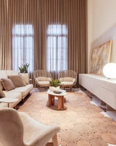 Sala de estar com sofá e poltronas em tons neutros, tapete de fibras naturais e cortina neutra