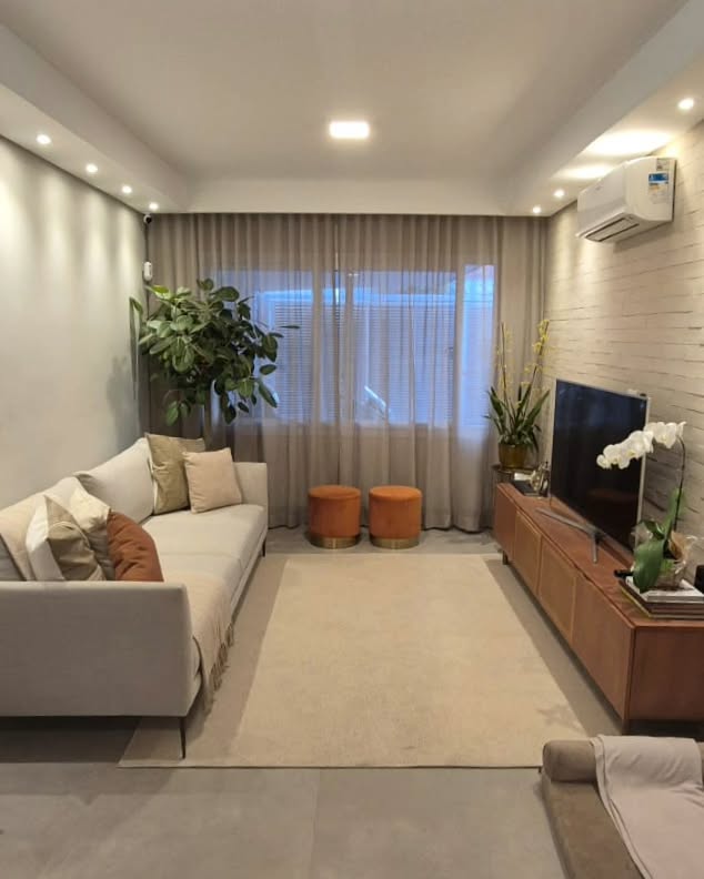 Sala de estar com sofá claro, pufes terracota e cortinas claras