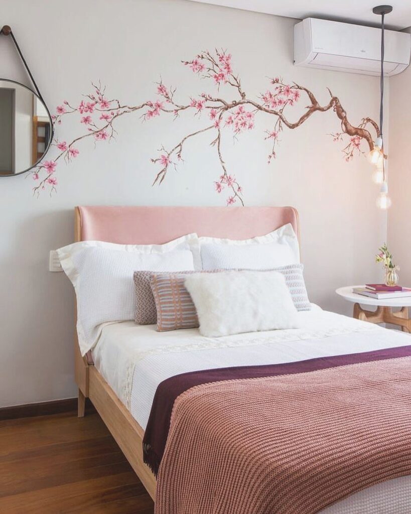 Quarto feminino com paredes brancas, cama com cabeceira e roupa de cama rosa e flores de cerejeira na parede