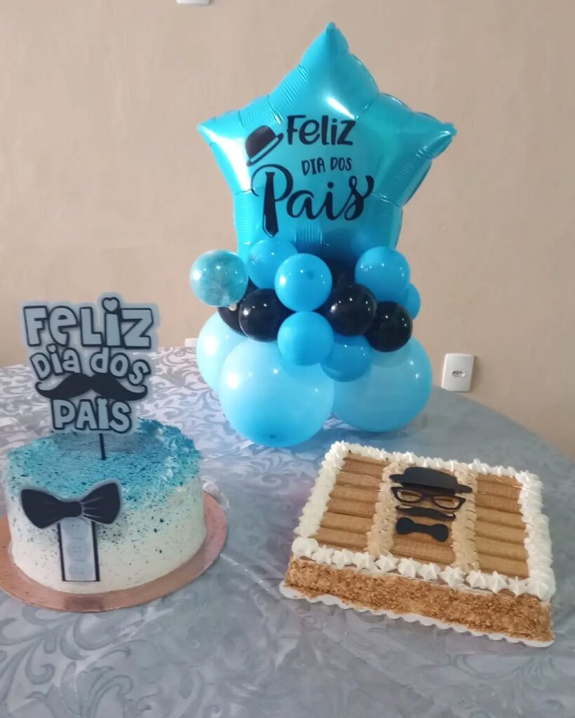 Mesa com balões azuis, bolos com frases e rosto com óculos e bigode