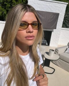 Sofia Grainge com blusa branca, cabelo loiro e óculos