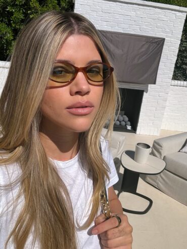 Sofia Grainge com blusa branca, cabelo loiro e óculos