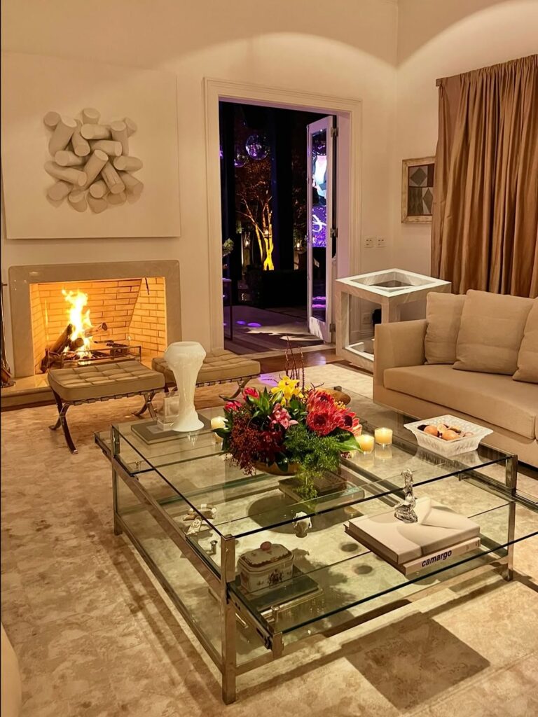 Sala de estar em tons neutros com lareira à lenha e mesa de vidro