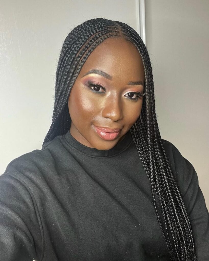 Mulher de pele preta, com blusa preta, cabelo trançado e maquiagem elegante