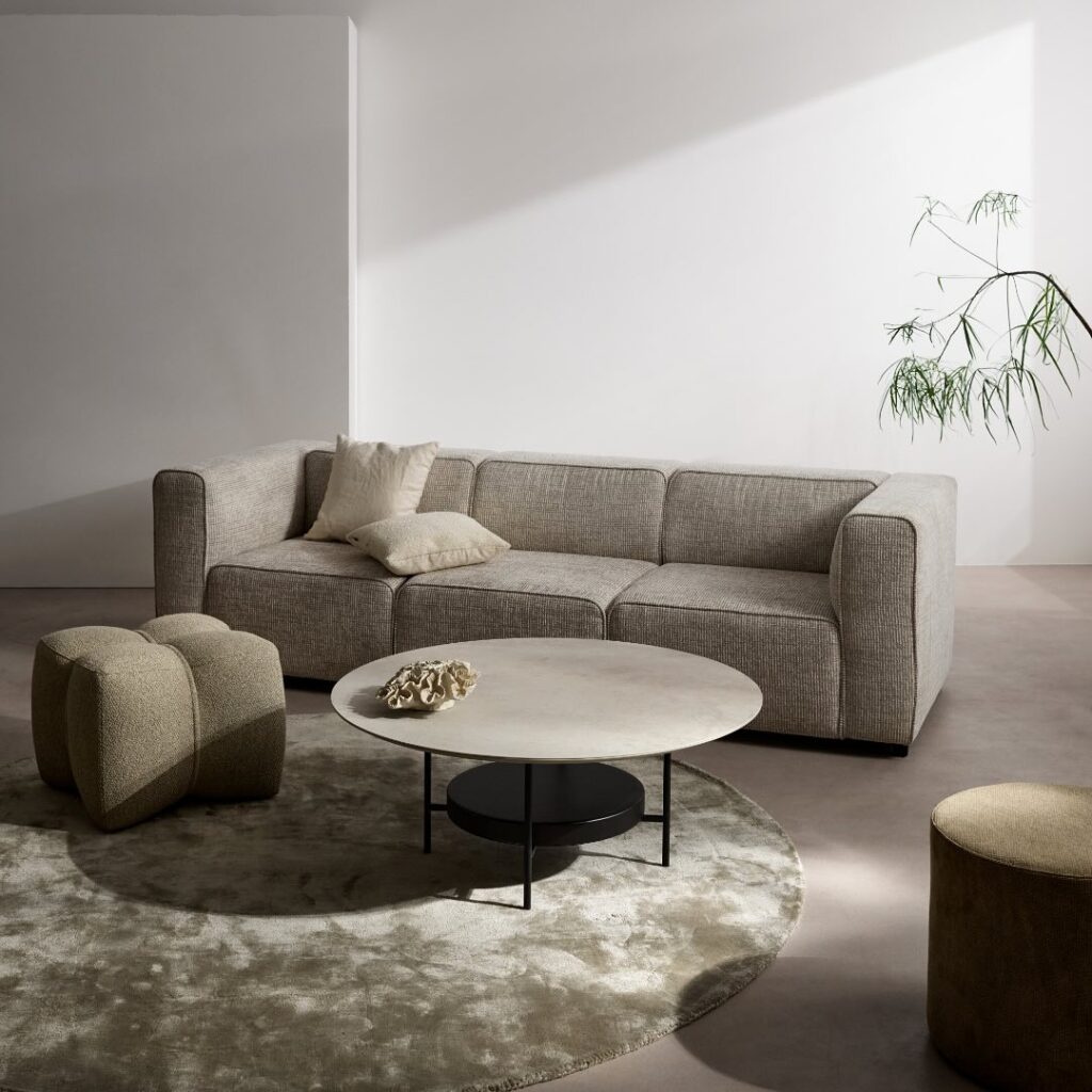 Sala com sofá cinza, mesa de centro redonda com base clara e pufe com design diferente
