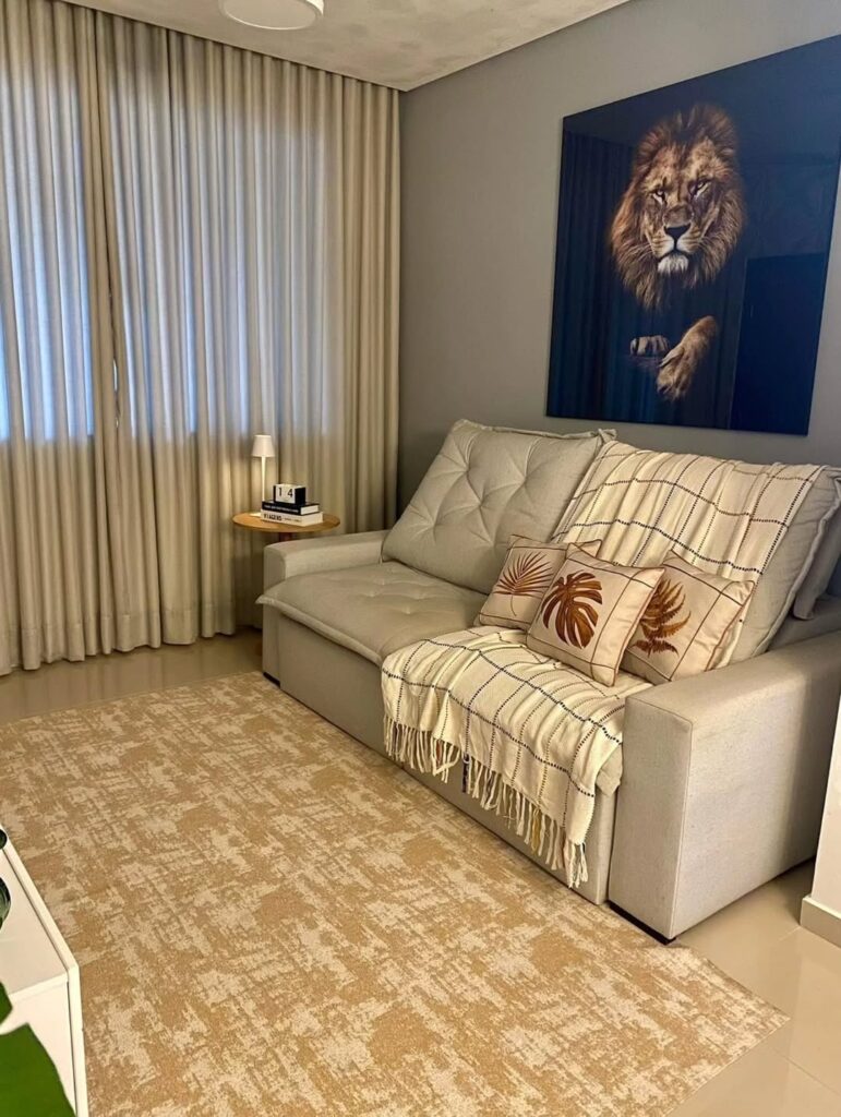 Sala com sofá de dois lugares cinza-claro com almofadas e manta xadrez e quadro com leão na parede
