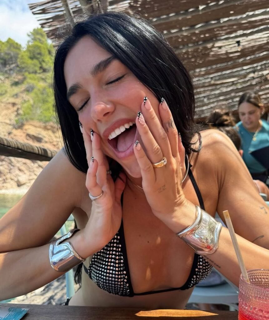 Dua Lipa com cabelo escuro e unhas decoradas com estampa de poá 