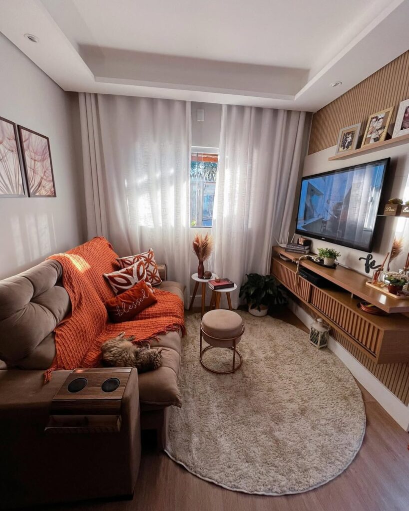 Sala com sofá e tapete em tons de marrom, cortina branca e quadros na parede