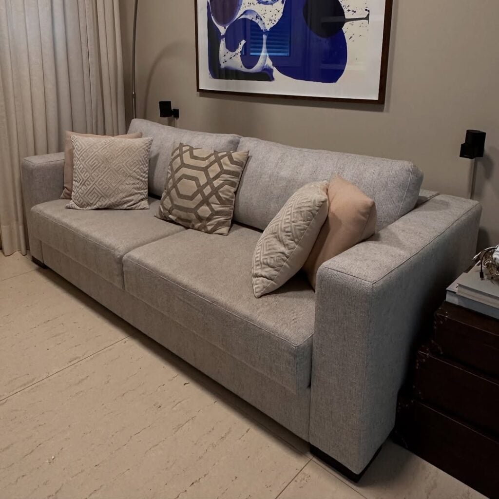 Sala com sofá cinza em linhas retas, almofadas e quadro branco com azul na parede