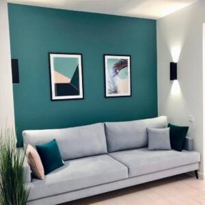 Sala com parede em tom de azul com sofá cinza-claro de linhas retas e pés palito