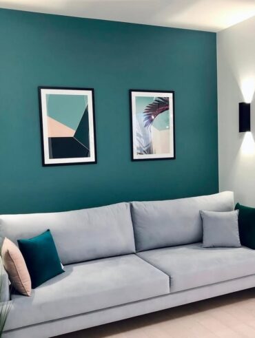 Sala com parede em tom de azul com sofá cinza-claro de linhas retas e pés palito