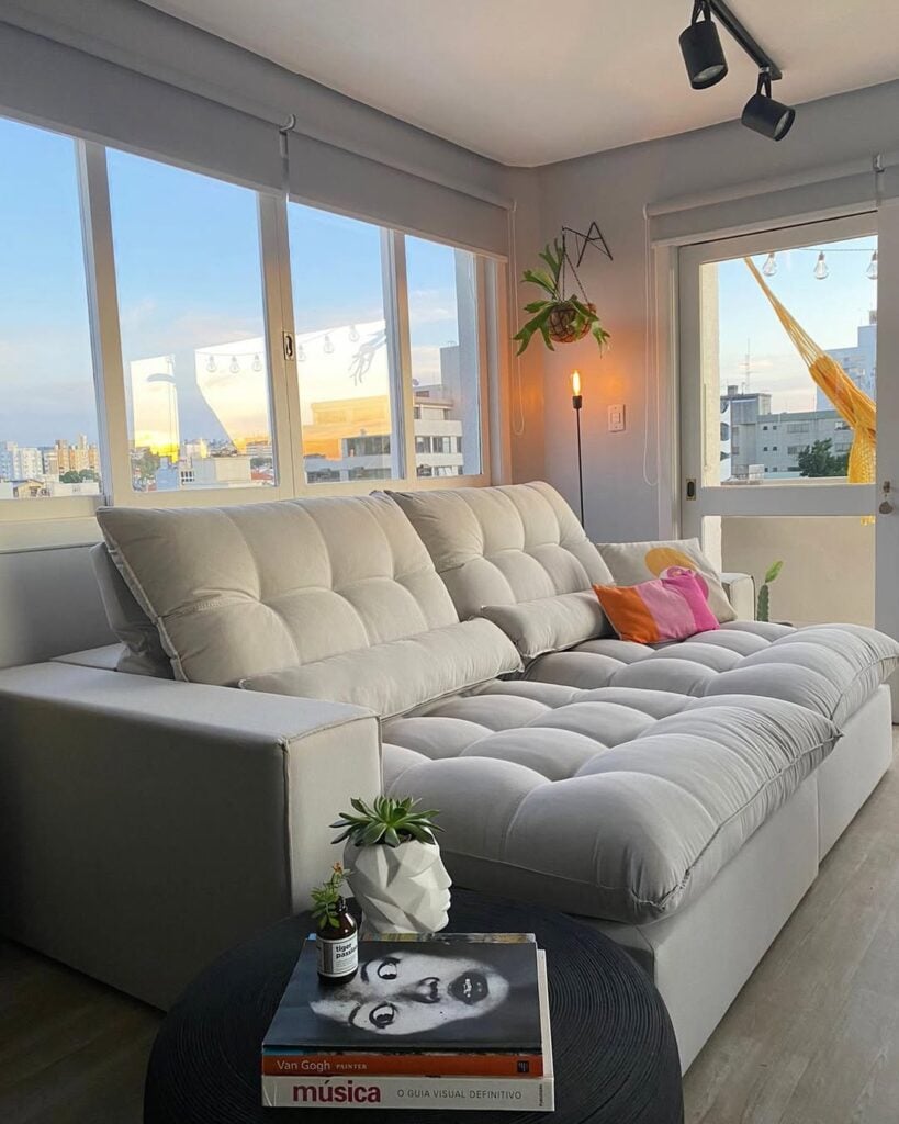 Sala de estar com sofá grande e espaçoso em cinza-claro, mesa lateral com livros