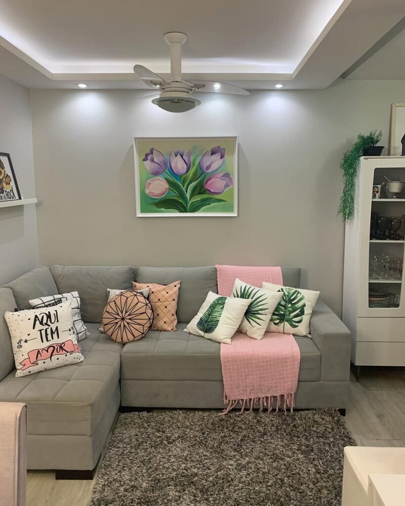 Sala com sofá cinza em formato de L, com almofadas coloridas e manta rosa