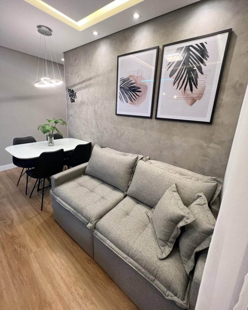 Sala com sofá cinza-claro, mesa de jantar branca com cadeiras pretas e quadros na parede