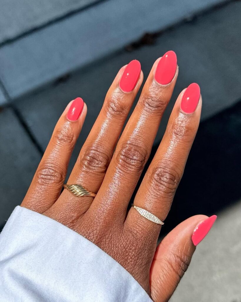 Mão de pele preta, com anéis em dourado e unha amendoada coral