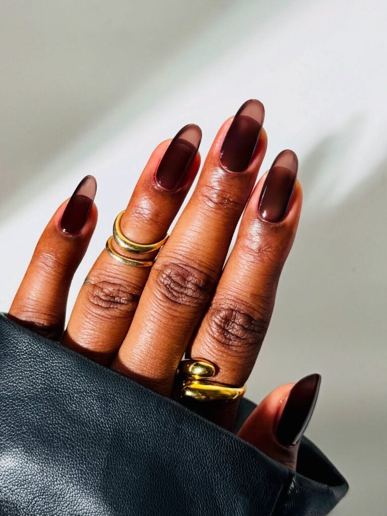 Mão de pele preta, com anéis em dourado e unha amendoada marrom
