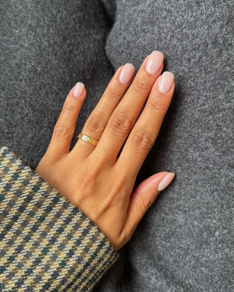 Mão de pele clara, com anel dourado e unha squoval nude