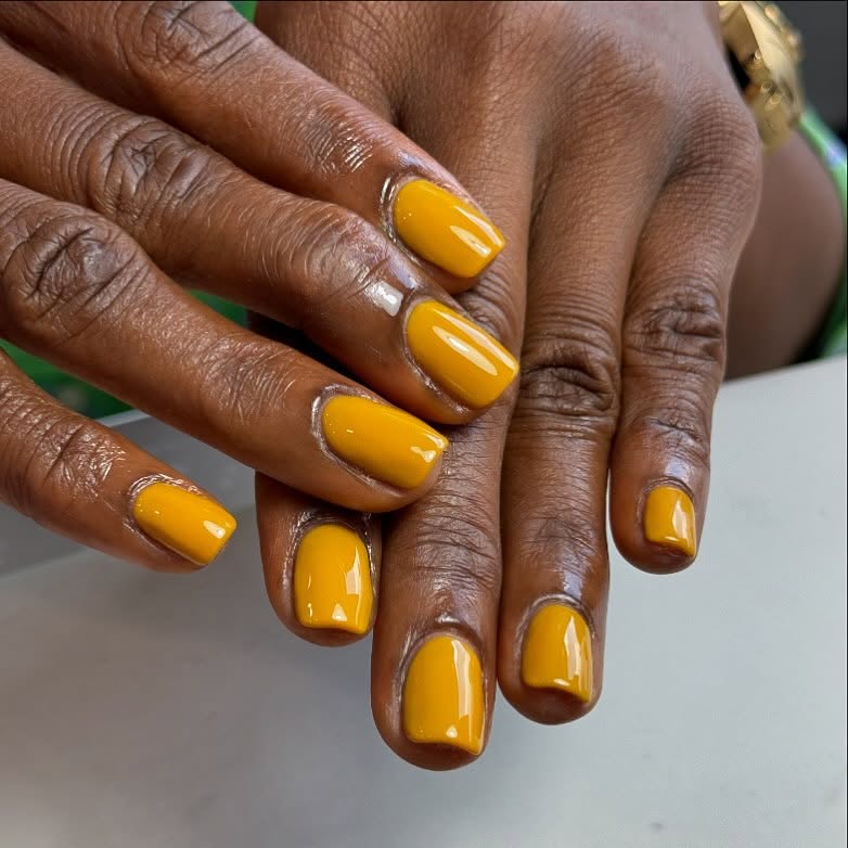 Mãos de pele preta, com unha quadrada pintada com esmalte mostarda