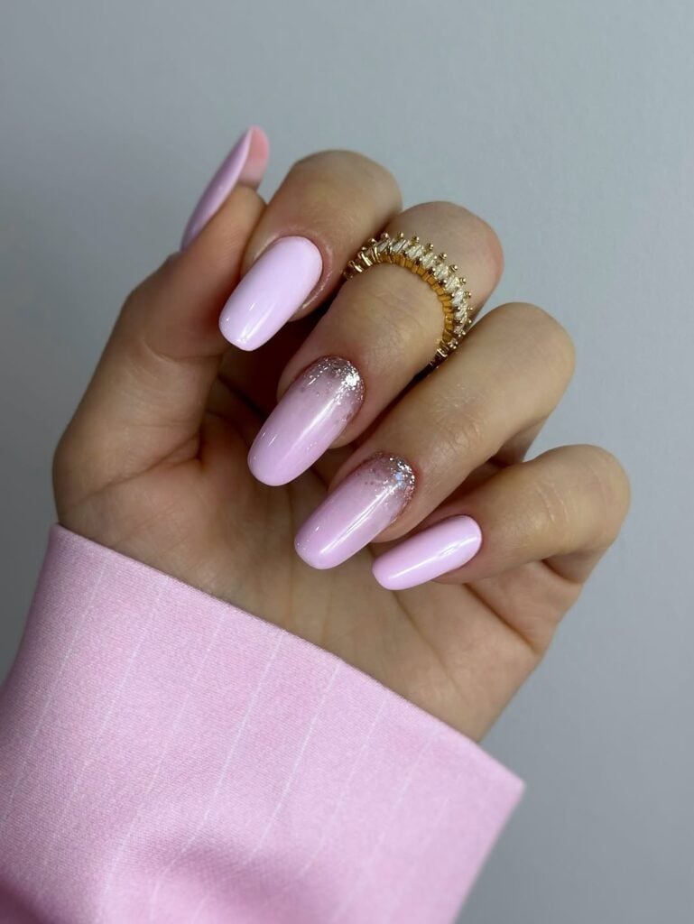 Mão de pele cara, com anel de brilhante e unha amendoada rosa-claro com glitter