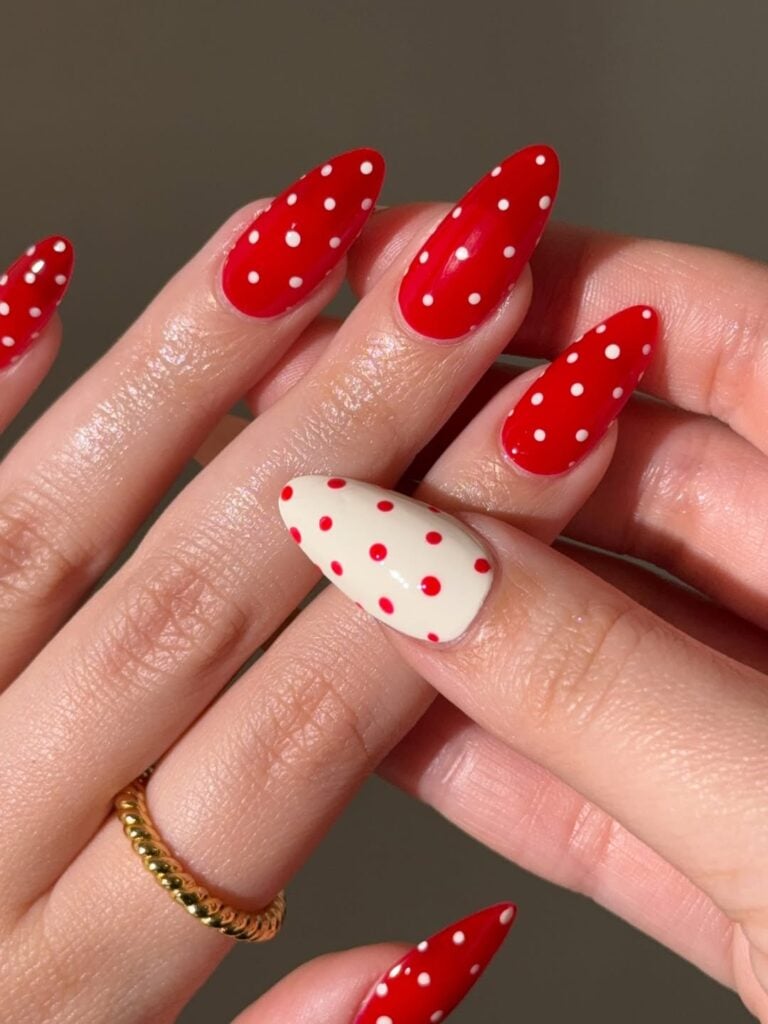 Mãos de pele clara, com anel em dourado e unhas poá em vermelho 