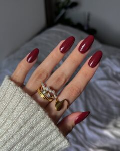 Mão de pele clara, com anéis em dourado e unha amendoada vinho