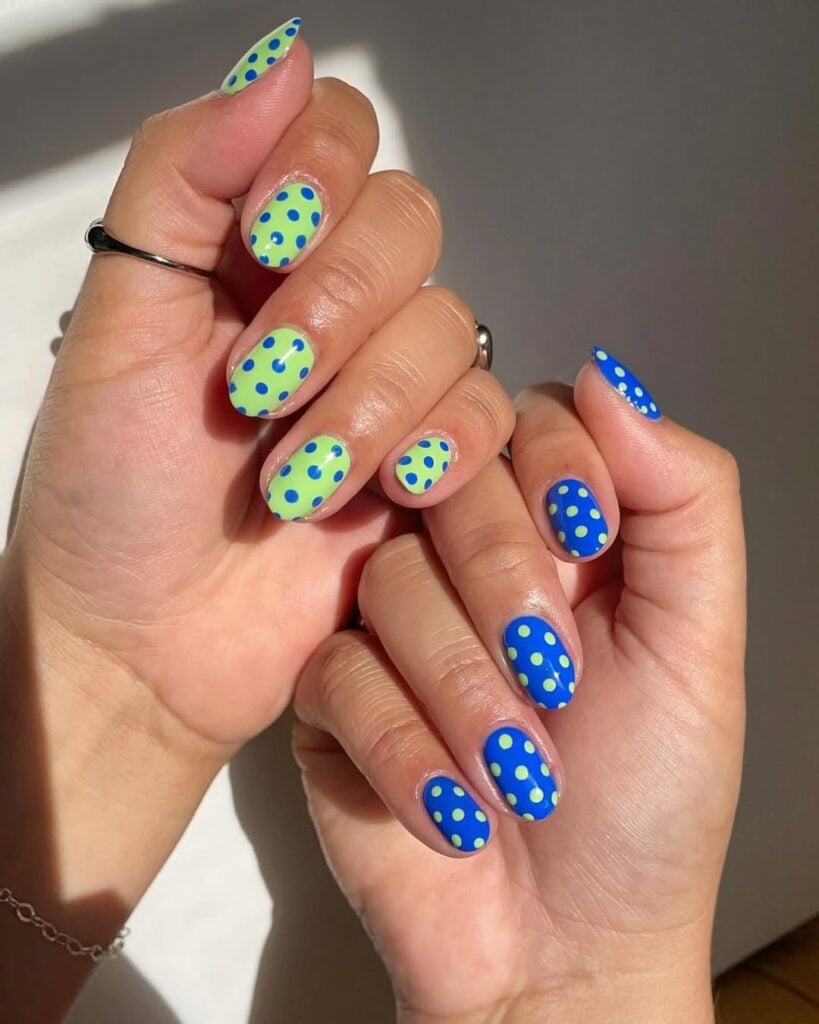 Mãos de pele clara, com anéis em prata e unhas decoradas com poá 