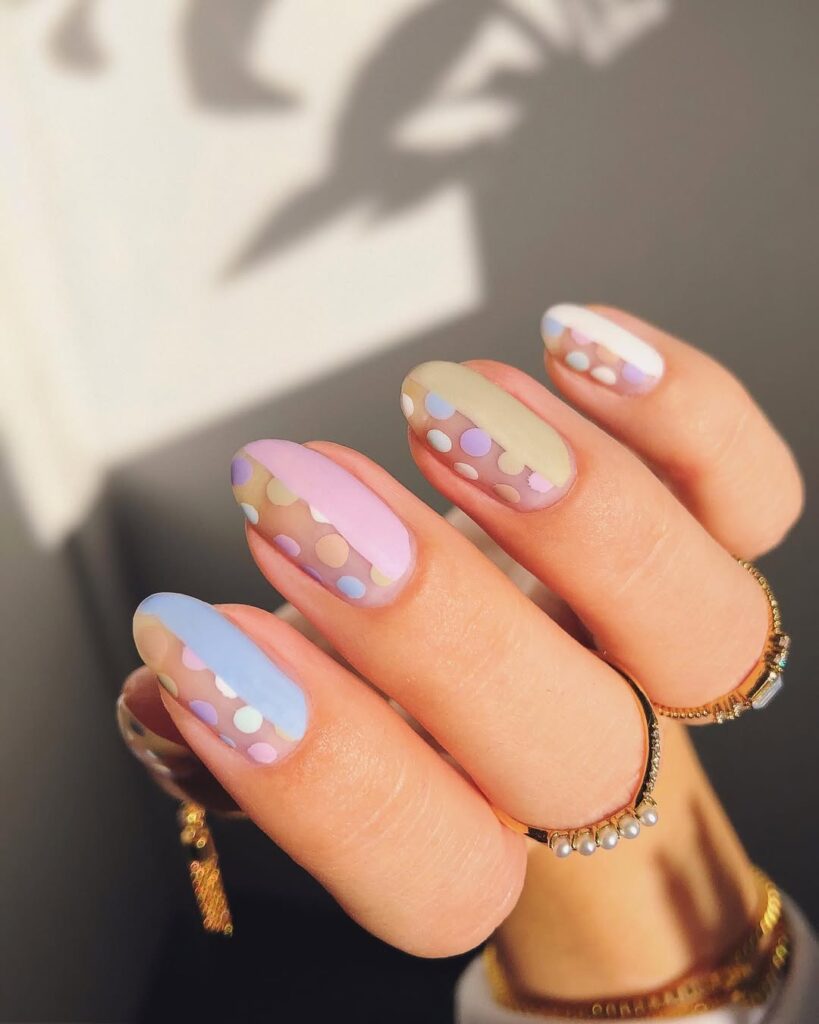 Mão de pele clara, com acessórios em dourado e unha amendoada em tons pastel com poá 