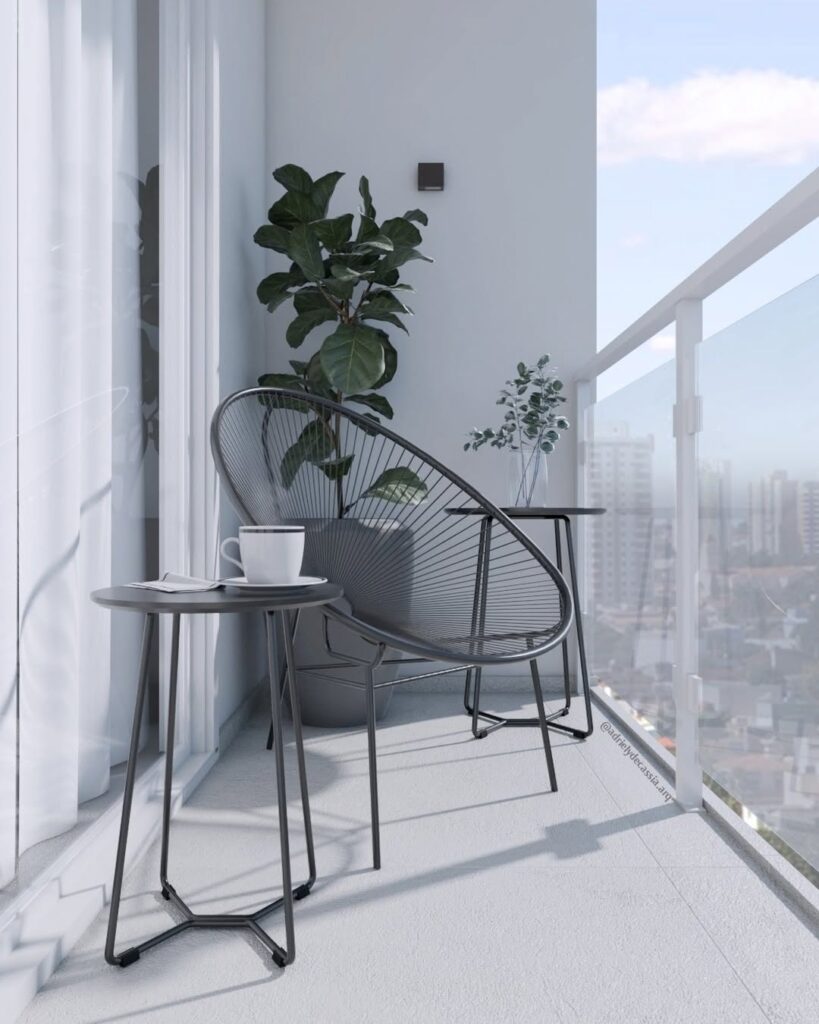 Varanda com parede e piso claro, poltrona e mesas de metal cinza-escuro e vaso com plantas