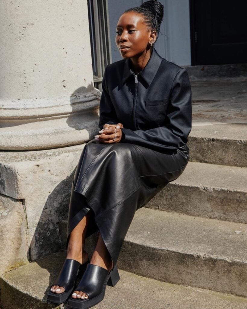 Mulher jovem com look all black e saia de couro longa