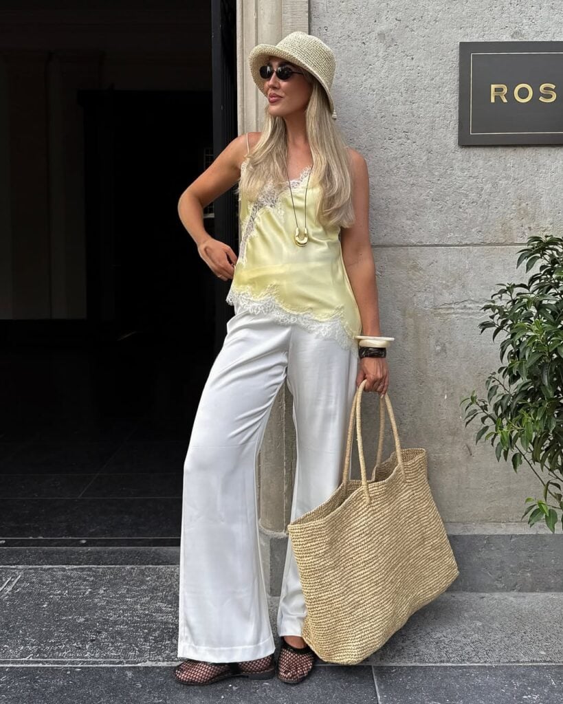 Mulher jovem, loira e de pele clara com calça branca, regata amarela e sapatilha telada