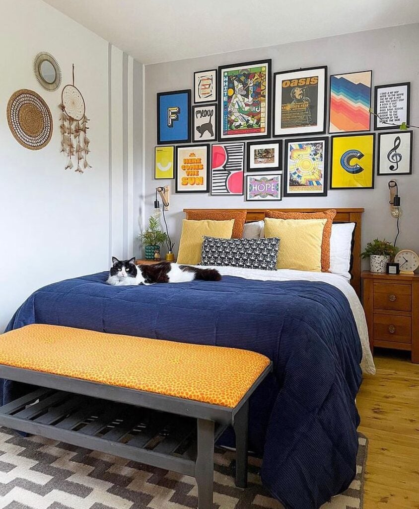 Quarto de casal com cama de madeira, quadros acima da cabeceira e luminárias nas paredes