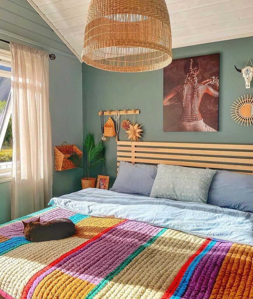 Quarto com cama de madeira, colcha colorida com gato, parede em tom de verde e luminária de fibras naturais