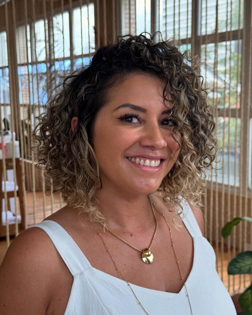 Mulher de pele clara, com roupa branca e cabelo curto cacheado com corte short bob