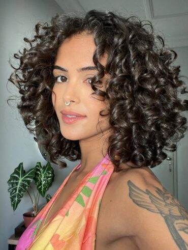 Mulher de pele preta-clara, com blusa estampada e cabelo crespo preso em camadas